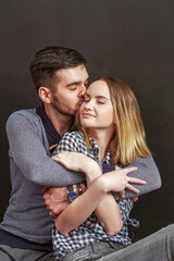 Bearded man kissing and hugging his sweetheart while sitting against of black background