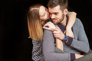 Beautiful couple sitting indoors and hugging against of black background