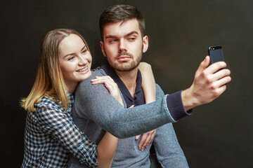 Couple of blonde woman and bearded man making selfie against of black background. Studio shot