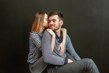 Beautiful young woman embracing her bearded boyfriend while sitting against of black background. Studio shot