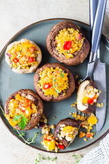 Baked stuffed portobello mushrooms with bulgur pilaf and chopped vegetables. Delicious and nutritious vegetarian dish. Stone background, selective focus. Top view.