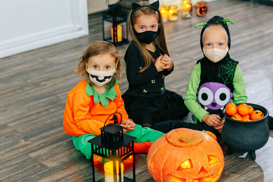 kids in carnival costumes are celebrating Halloween, wearing face masks and playing with pumpkins and candies indoors