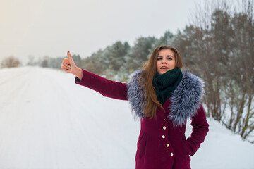 Fototapeta na wymiar young beautiful girl hitchhiker catches car on winter road