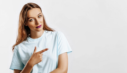 Portrait of a smiling girl pointing finger to the side at on a white isolated background. A woman points to an idea, a place for advertising. Positive girl with fashion make-up with purple lips.