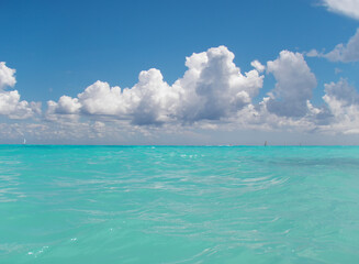 View over the surface of the water of the Caribbean Sea, in the background sailing boats, the blue sky, and white clouds. Playa del Carmen, Mexico