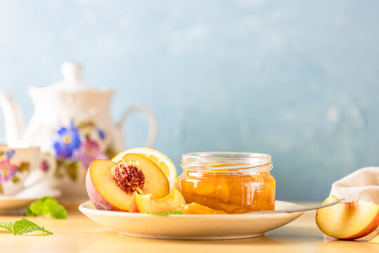 Fresh homemade peach jam in glass jar on a wooden background. Several fresh berries, mint and all for tea party are near it.