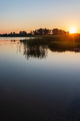 Fototapeta premium Sunrise over lake on a calm, peaceful morning, with forest in afar