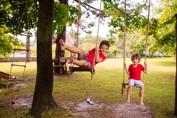 Two cute caucasian brother boys in red T-shirts are swinging on a swing in the park