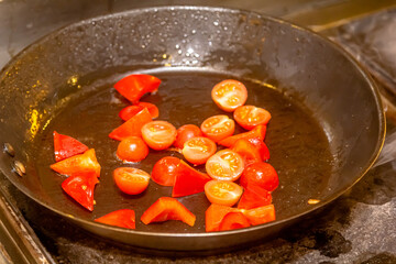 Halves of tomatoes and slices of pepper are fried in a frying pan.
