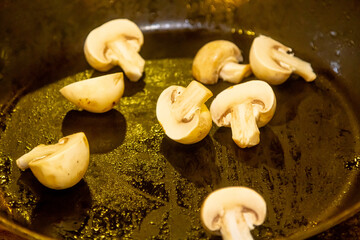 Halves of mushrooms are fried in oil in a frying pan.