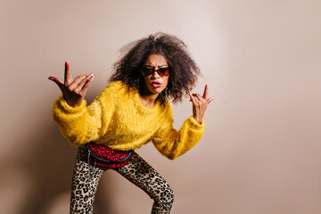Wonderful young woman with funny hairstyle posing on brown background. Magnificent black-haired african girl fooling around in studio.