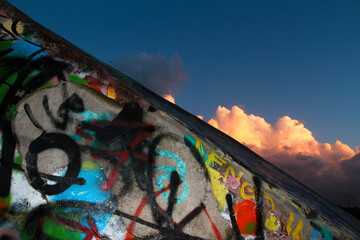Close up of very colorful graffiti on the wall, in the background clouds reddened by the setting sun.