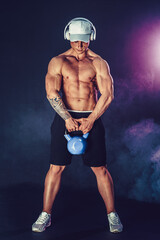 Fototapeta na wymiar Muscular bodybuilder doing Exercise with kettlebell. Studio shot with smoke.