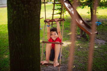 Obraz premium A beautiful little caucasian boy on a wooden ladder for children in the park. A day in nature