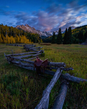 Saddle on split rail fence against Mount Sneffels during sunrise