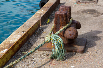 A bollard at a dockside with the rope of a boat tied around it to keep the boat moored to the jetty