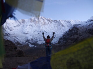 A climber with her arms up on the other side of Talcho (Tibetan praying flags), ABC (Annapurna Base Camp) Trek, Annapurna, Nepal