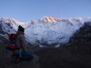 Fototapeta na wymiar A climber sits on a rock and watches the sunrise over a snow-covered rock, ABC (Annapurna Base Camp) Trek, Annapurna, Nepal