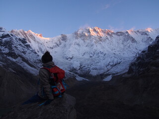 Fototapeta premium A climber sits on a rock and watches the sunrise over a snow-covered rock, ABC (Annapurna Base Camp) Trek, Annapurna, Nepal
