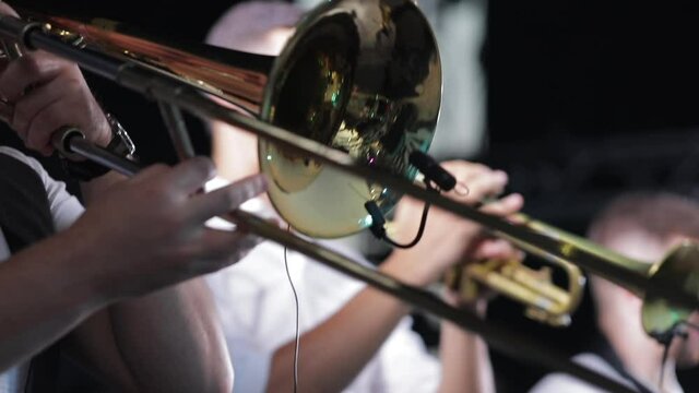 The musician plays the trombone with the band on stage, close up from the side. 