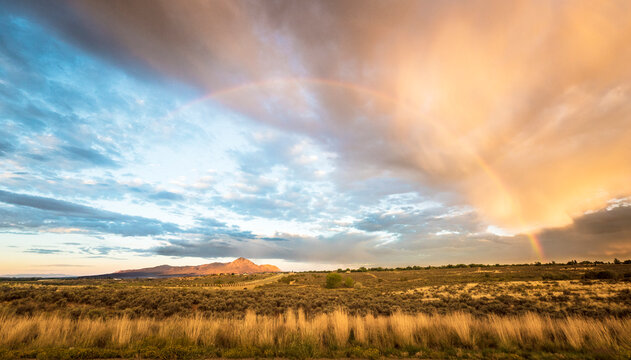 Scenic view of rainbow over grassy landscape and Sleeping Ute Mountain