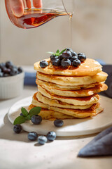 Maple syrup is pouring on homemade pancakes, fresh blueberries. Healthy American breakfast or brunch, favorite meal.