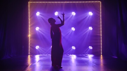 Silhouette a young girl dancer in a red sari. Indian folk dance. Shot in a dark studio with smoke and neon lighting.
