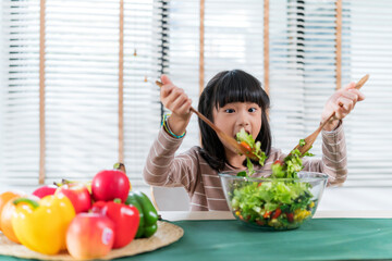 Asian happy girl enjoying time doing vegetables salad in kitchen room