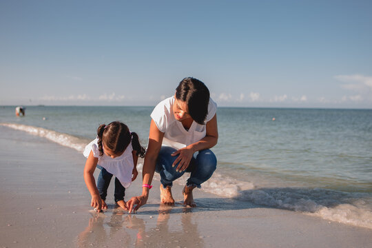 Mom and daughter on the beach picking up seashells and having fun  stock photo 