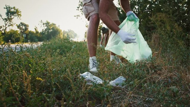 Millennial people picking up litter along road, ecology and volunteering concept, close up