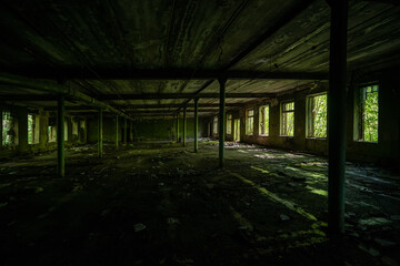 The interior of an empty old abandoned industrial building with garbage on the floor, columns and rows of broken windows