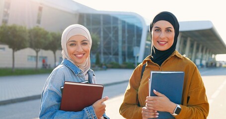 Portrait young Arabic beautiful women in headscarves smiling and holding textbooks books. Pretty...