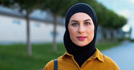 Portrait of young Arabian beautiful woman in black hijab standing at street and smiling to camera....