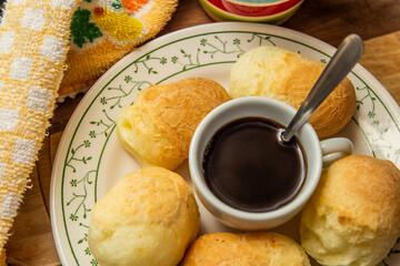 Uma xícara de café com pães de queijo dentro de um prato.