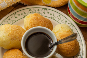 Uma xícara de café com pães de queijo ao redor dentro de um prato.