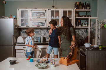 A beautiful caucasian  mother in a dress with her two sons is standing in the kitchen during breakfast. Family time