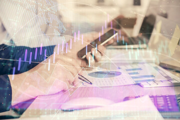 Double exposure of man's hands holding and using a digital device and forex graph drawing. Financial market concept.