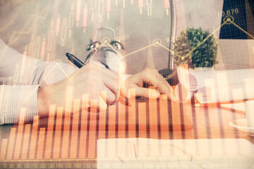 Double exposure of man's hands holding and using a phone and financial graph drawing. Analysis concept.