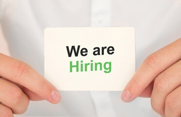 Man's hands take a card with words We are hiring, finance and business concept.