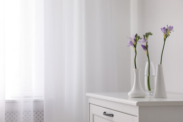 Fototapeta na wymiar Beautiful spring freesia flowers on white chest of drawers in room, space for text
