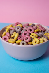 Isolated bowl of mixed cereals and marshmallows on a blue and pink background