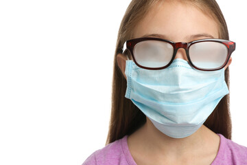 Little girl with foggy glasses caused by wearing disposable mask on white background, closeup. Protective measure during coronavirus pandemic