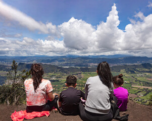 Two young women with two kids admiring the beautiful mountain landscape at the top of the mountain with green valley, blue mountains and blue sky at background, Trekking and camping concept