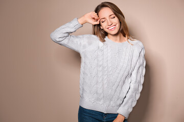 Happy young woman wearing warm sweater on beige background