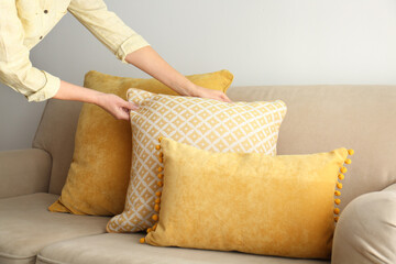 Woman arranging pillows on sofa, closeup view. Interior design
