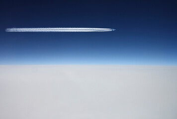 Fototapeta premium Airplane flys above white clouds in a deep blue sky and leaving jet trail