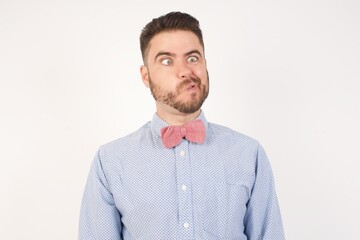 Portrait of European man dressed in formal shirt and bow tie poses against white background making grimace and crazy face, screaming out of control, funny lunatic expressing freedom and wild.