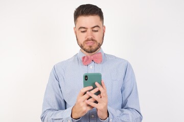 Portrait of excited European man dressed in formal shirt and bow tie poses against white background...