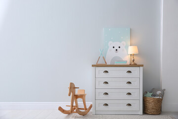 Modern white chest of drawers near light wall in child room, space for text. Interior design