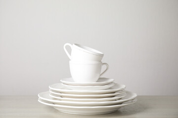 Stack of clean plates and cups on table against white background